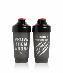 Two dark gray shaker bottles with black caps and red lids, standing side by side on a white background. The left bottle has the text 'PROVE THEM WRONG' in white, and the right bottle has 'HUMBLE UNDERDOGS' with a white claw graphic.